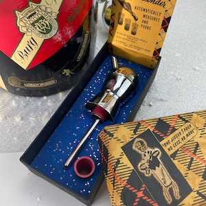 May include: A silver cocktail jigger with a red rubber stopper in a blue and silver box. The box has a label that reads "The Famous Mr. Bartender Automatically Measures and Pours". The box also has a label that reads "One Jigger I Pour No Less, No More".