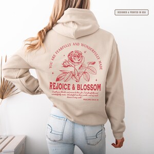 May include: Beige hoodie with a red rose graphic and the text "You are fearfully and wonderfully made. Rejoice & Blossom. I will give thanks and praise to thee, for I am fearfully and wonderfully made. Wonderful are thy works, and my soul knows it very well. Psalms 139:14-18."