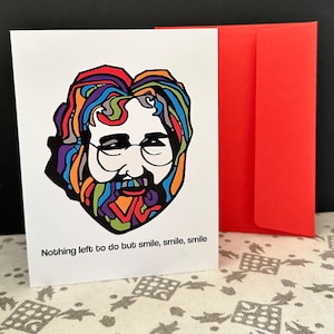 May include: A white greeting card with a colorful illustration of a man with glasses and a beard. The card is accompanied by a bright red envelope. The text on the card reads, "Nothing left to do but smile, smile, smile."