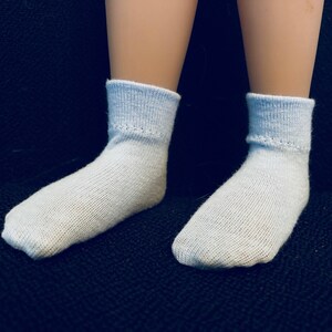 Puede incluir: Un par de calcetines de color azul claro en los pies de una mu&ntilde;eca. Los calcetines est&aacute;n hechos de un material suave y c&oacute;modo y tienen una textura acanalada.