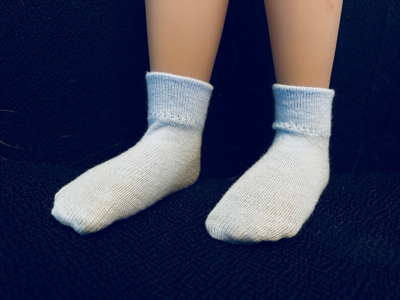 Puede incluir: Un par de calcetines de color azul claro en los pies de una mu&ntilde;eca. Los calcetines est&aacute;n hechos de un material suave y c&oacute;modo y tienen una textura acanalada.