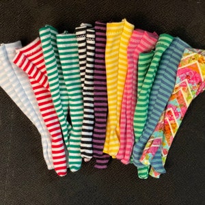 May include: A collection of colorful knee-high socks with various striped patterns. The socks feature stripes in light blue, red, green, black, purple, yellow, pink, and teal. One sock has a floral design. These socks are made of a soft, stretchy material.