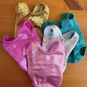 May include: A collection of five metallic leotards in various colors, including gold, pink, silver, and teal. Each leotard has a scoop neck and a shimmering, textured surface, suggesting a dance or gymnastics theme.