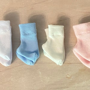 May include: Four pairs of folded socks in different colors: light blue, white, pink, and light blue. The socks are all folded in the same way, with the toes facing up.