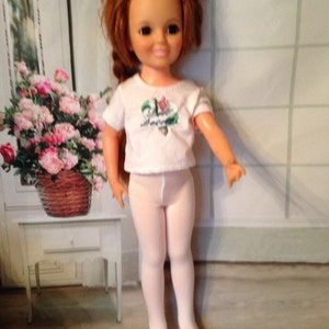 May include: A vintage doll with red hair wearing a white t-shirt with a floral design and white tights.