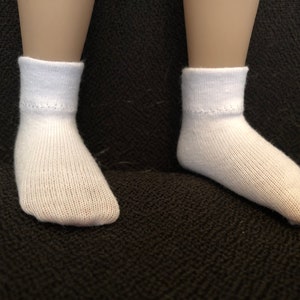 Puede incluir: Un par de calcetines blancos hasta el tobillo con textura acanalada. Los calcetines est&aacute;n sobre una superficie de tela negra.