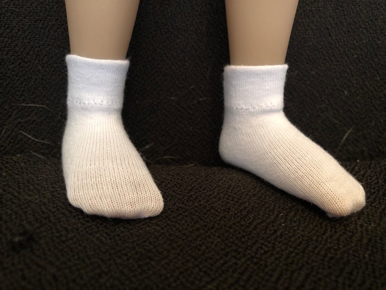 Puede incluir: Un par de calcetines blancos hasta el tobillo con textura acanalada. Los calcetines est&aacute;n sobre una superficie de tela negra.