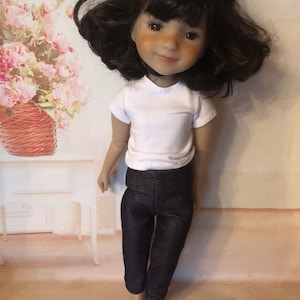 May include: A doll with brown hair wearing a white t-shirt and dark blue denim pants.