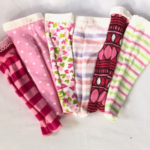 May include: A set of six pairs of pink and white patterned leggings. The leggings have different patterns, including polka dots, stripes and hearts.