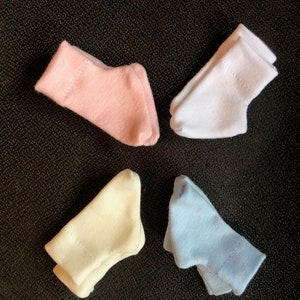 May include: Four pairs of socks in different colors: pink, white, cream, and light blue. The socks are folded and arranged on a dark textured surface.