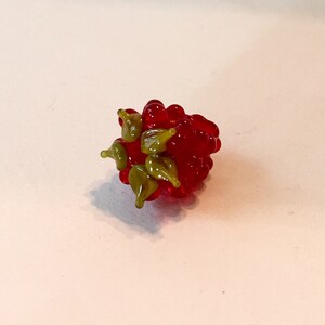 Pode incluir: Uma escultura de framboesa de vidro artesanal. A escultura apresenta um aglomerado de esferas vermelhas transl&uacute;cidas, com detalhes de folhas verdes. A framboesa de vidro &eacute; um item decorativo, perfeito para decora&ccedil;&atilde;o de casa ou como um presente &uacute;nico.