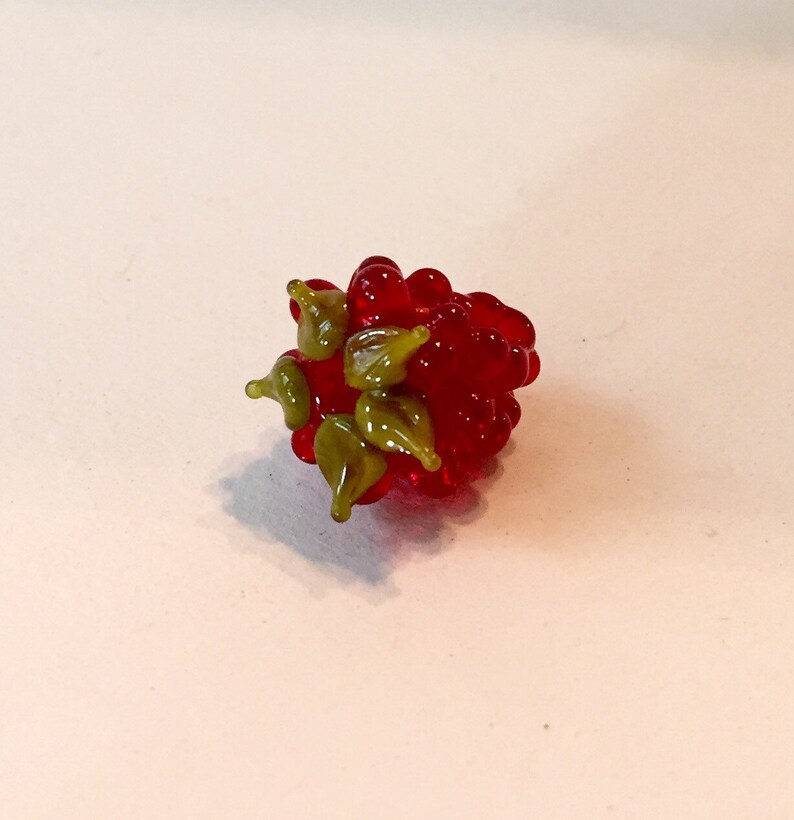 Pode incluir: Uma escultura de framboesa de vidro artesanal. A escultura apresenta um aglomerado de esferas vermelhas transl&uacute;cidas, com detalhes de folhas verdes. A framboesa de vidro &eacute; um item decorativo, perfeito para decora&ccedil;&atilde;o de casa ou como um presente &uacute;nico.