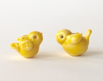 Può includere: Due piccole statuine di uccelli in ceramica gialla. Gli uccelli si guardano e hanno una finitura lucida.