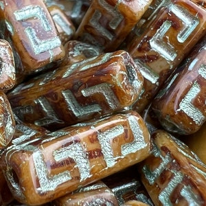 May include: A close-up of a pile of brown and silver rectangular beads with a geometric pattern. The beads are made of ceramic and have a glossy finish.