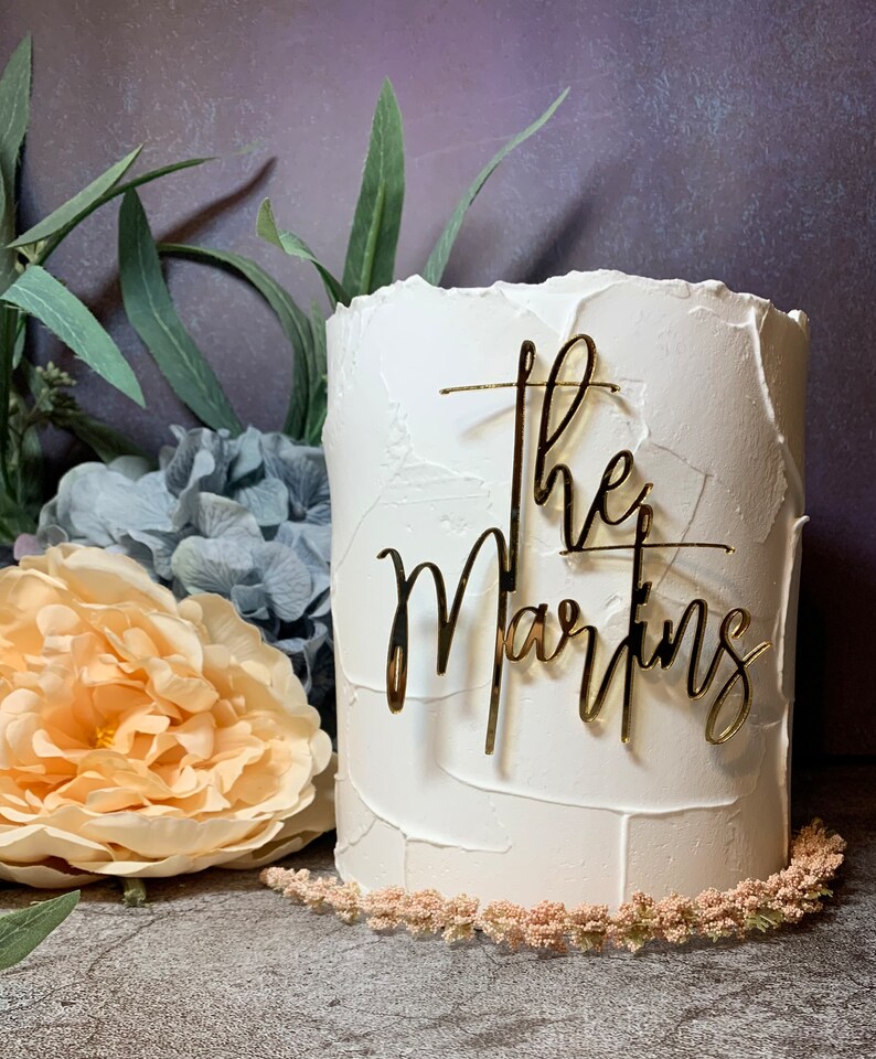 May include: A white cake with a gold glitter topper that says 'the Martins'.