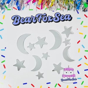 May include: A set of silver mirror acrylic shapes, including moons and stars, with a cake design featuring the text "Bear Fox Sea".