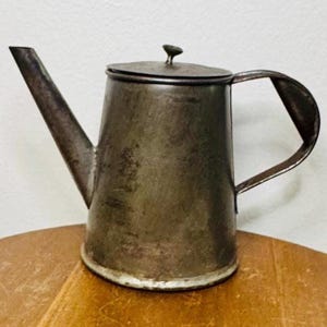 May include: A vintage metal teapot with a lid and a handle. The teapot is a dark gray color and has a worn, rustic look.