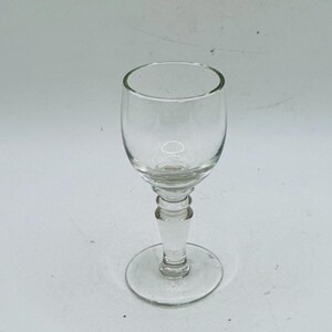 May include: A clear, stemmed glass with a rounded bowl and a detailed stem. The glass sits on a circular base. The glass is designed for serving beverages.