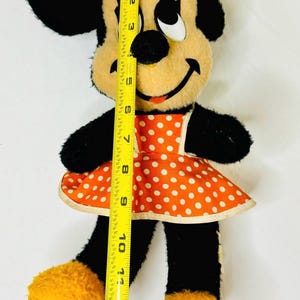 May include: Vintage Minnie Mouse plush doll, approximately 12 inches tall. The doll features black fur, a tan face, and an orange dress with white polka dots. A yellow bow adorns her head. The doll's feet are yellow.