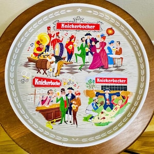 May include: Round serving tray with a wooden rim and a decorative illustration. The illustration features several scenes with people, musicians, and the text "Knickerbocker" in red banners. The tray has a white and gray border.