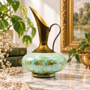 May include: A decorative pitcher featuring a wide, rounded glass base with a mottled light blue and green finish. The top section is crafted from polished brass, including a tall, tapered spout and a curved handle attached to the neck.