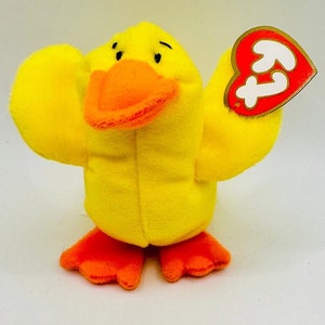 May include: Yellow plush duck with an orange beak and feet. The duck is holding a red heart-shaped tag with the word "Ty" on it.