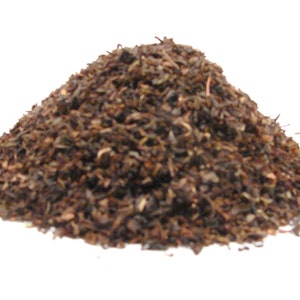 May include: A pile of loose leaf tea, with a mix of dark brown and green hues. The tea leaves are finely cut and appear to be a blend, suitable for brewing a flavorful cup. The image is set against a plain white background.