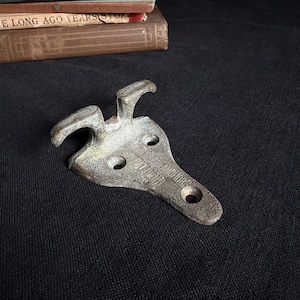 May include: A weathered, cast metal nautical cleat with a dual-horn design and a triangular base featuring three mounting holes. The surface displays a textured, aged patina with visible embossed text reading "NORTHILL ANCHORS PAT PEND".