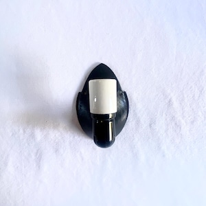 May include: A black wall sconce with a leaf-shaped backing. The sconce features a white cylindrical shade and a black base. The fixture is designed for a single light bulb and is suitable for indoor use.