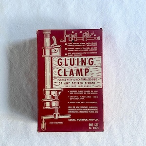 Puede incluir: Caja de abrazadera de encolado vintage en burdeos y crema. La caja presenta una ilustración detallada de la abrazadera y las palabras "Gluing Clamp". El texto en la caja describe las características de la abrazadera y su uso.
