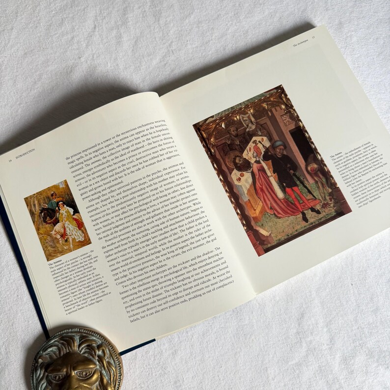 May include: An open book with text and illustrations. The pages are white with black text and colourful images. A brass lion head is at the bottom of the image. The book is open on a white surface.