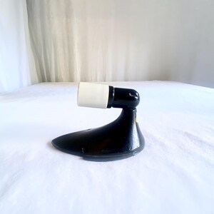 May include: A black and white vintage light fixture. The fixture has a black base with a curved design and a white cylindrical socket. The fixture is designed to hold a light bulb. The fixture is likely made of metal.