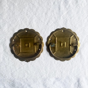 Puede incluir: Dos tiradores de cajón antiguos de latón con un diseño de borde festoneado. Cada tirador presenta un centro cuadrado con un pequeño cuadrado en el medio y un asa curva. El latón tiene una pátina cálida y envejecida.