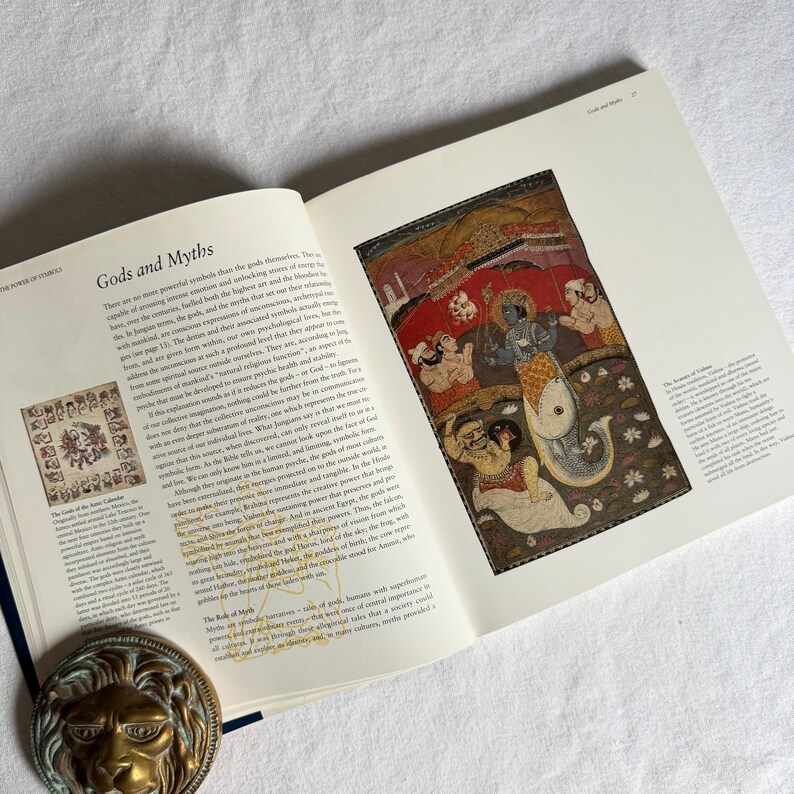 May include: An open book titled "Gods and Myths" with a vibrant illustration on the right page. The image depicts figures and a fish-like creature. A brass lion head is visible at the bottom left corner.