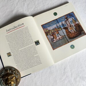 May include: An open book displaying the title "Introduction" on the left page. The right page shows a vibrant illustration of a ship and figures. The book rests on a white surface, with a decorative lion head in the lower left corner.