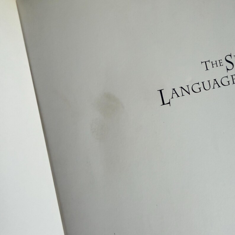 May include: A close-up of a white page with the words "THE LANGUAGE" printed in black. The page has a light brown stain on the right side. The page is slightly angled.