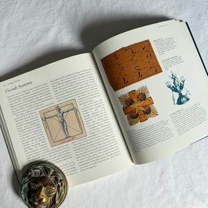 May include: An open book displaying the title "Occult Systems" and various esoteric illustrations. A brass lion's head bookend is placed on the page. The book contains diagrams and text related to occultism and spiritual practices.