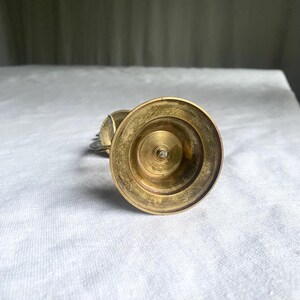 May include: A vintage brass candlestick holder with a wide, circular base and a central spike. The candlestick has a warm, golden hue and shows signs of age. The design is simple and elegant, suitable for various decor styles.