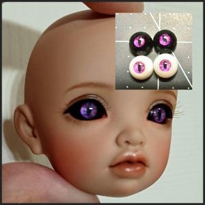 Puede incluir: Un par de ojos de mu&ntilde;eca de color morado y negro con iris blanco. Los ojos se muestran en la cara de una mu&ntilde;eca y tambi&eacute;n en una superficie negra.