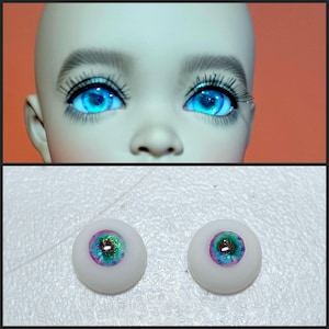 May include: Two blue doll eyes with iridescent green and purple flecks. The eyes are on a white background.