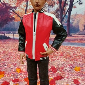 Pu&ograve; includere: Una bambola che indossa una giacca di pelle rossa e nera con dettagli bianchi, jeans neri e scarpe da ginnastica rosse. La bambola &egrave; in piedi su un letto di foglie rosse e arancioni.