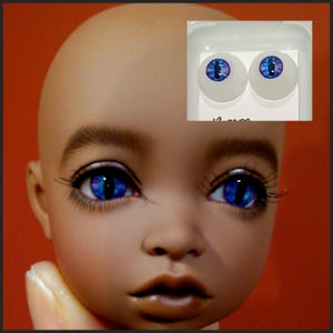 Puede incluir: Un par de ojos de mu&ntilde;eca azules y morados con iris blanco y pupila negra. Los ojos est&aacute;n en un paquete de pl&aacute;stico transparente con fondo blanco. El paquete tiene el texto "12 mm" impreso.