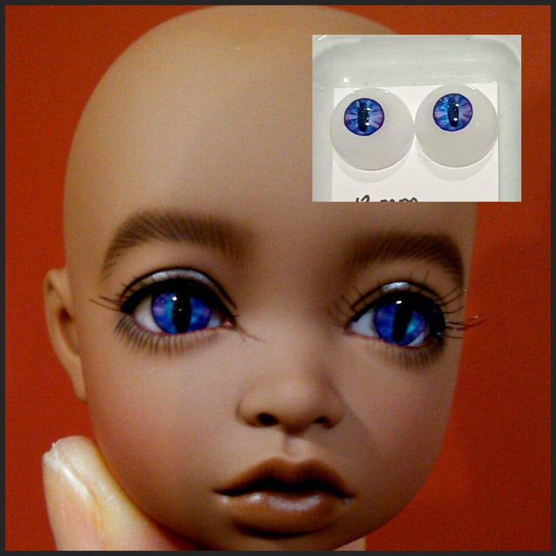 Puede incluir: Un par de ojos de mu&ntilde;eca azules y morados con iris blanco y pupila negra. Los ojos est&aacute;n en un paquete de pl&aacute;stico transparente con fondo blanco. El paquete tiene el texto "12 mm" impreso.