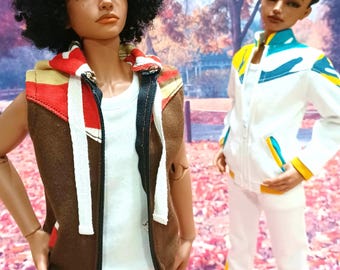 May include: Two fashion dolls wearing different outfits. The doll on the left is wearing a brown sleeveless hoodie with a white zipper and a white t-shirt underneath. The doll on the right is wearing a white jacket with blue and yellow accents. Both dolls have brown skin and short, dark hair.