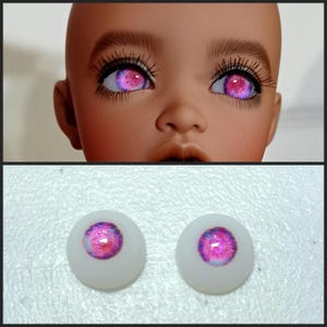 May include: Two pink and white doll eyes with a galaxy-like pattern. The eyes are on a white background.