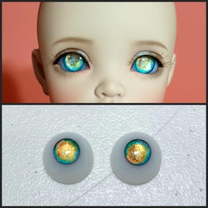May include: A pair of blue and gold doll eyes with a white iris and a gold flecked pupil. The eyes are set in a white plastic base.
