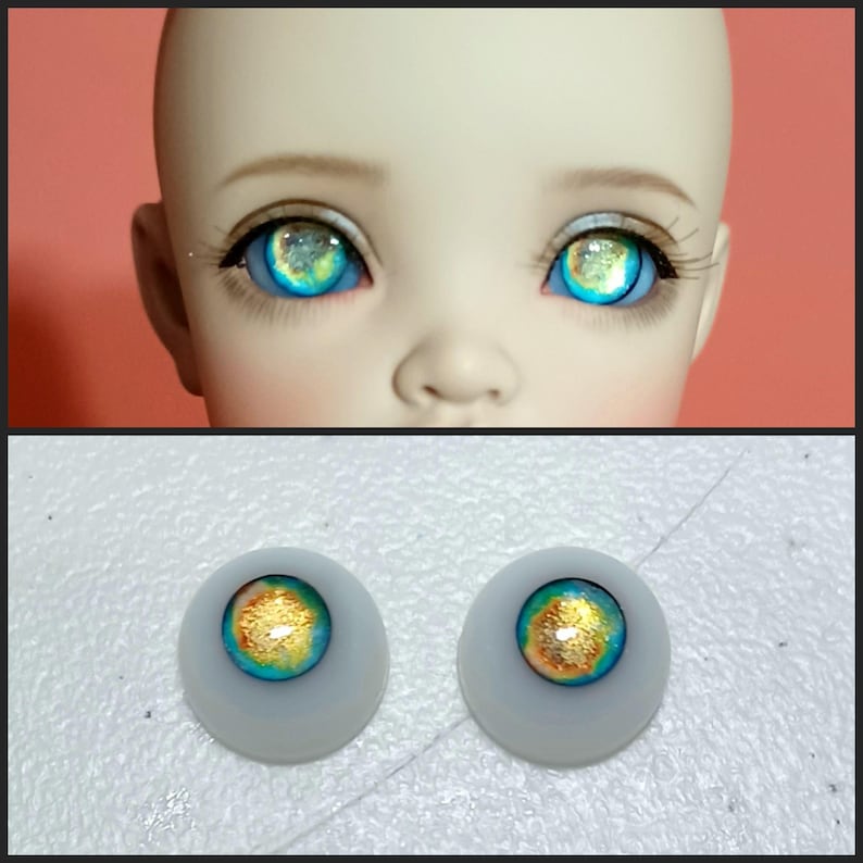 May include: A pair of blue and gold doll eyes with a white iris and a gold flecked pupil. The eyes are set in a white plastic base.