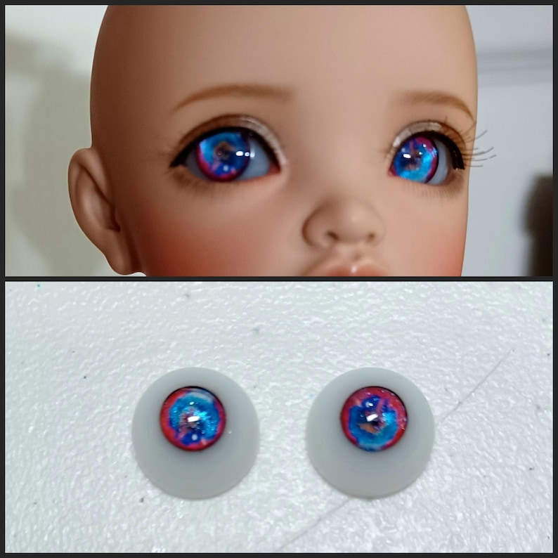 May include: A pair of blue and pink doll eyes with a white iris and a black pupil. The eyes are on a white background.