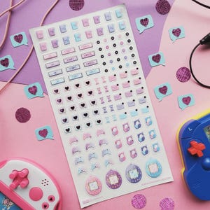 May include: A sheet of pastel-colored stickers featuring various icons, including hearts, speech bubbles, game controllers, and headphones. The stickers are in shades of pink, blue, and purple. The sheet also includes text labels like "OK", "Start", and "Cancel".
