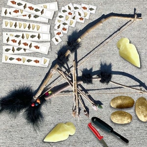 May include: A DIY bow and arrow set made from natural materials. The bow is made from a long, thin branch of wood, and the arrow is made from a shorter branch. The set also includes a small knife, a piece of string, and a few feathers. The bow and arrow are lying on a concrete surface.